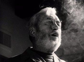 Movie still from “The Other Side of the Wind” (2018), directed by Orson Welles – An old man with a beard is smoking a cigarette; Close Up shot, Low angle