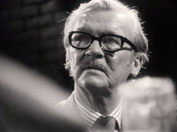Movie still from “The Other Side of the Wind” (2018), directed by Orson Welles – An older man wearing a suit and glasses; Close Up shot, Over the shoulder angle