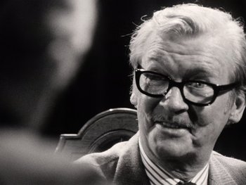 Movie still from “The Other Side of the Wind” (2018), directed by Orson Welles – An older man wearing a suit and glasses; Close Up shot, Over the shoulder angle