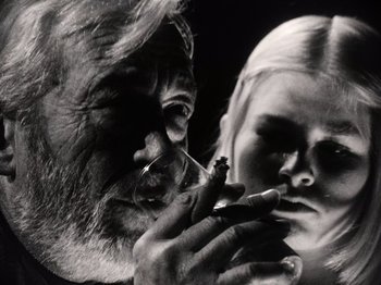Movie still from “The Other Side of the Wind” (2018), directed by Orson Welles – An old man smoking a cigarette next to a young woman; Extreme Close Up shot, Low angle