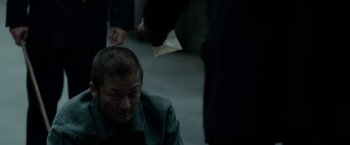 Movie still from “The Outsider” (2018), directed by Martin Zandvliet – A man sitting on the ground in a dark room; Close Up shot, Over the shoulder angle