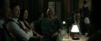 Movie still from “The Outsider” (2018), directed by Martin Zandvliet – A man sitting at a table with a drink in front of him; Medium shot, Low angle