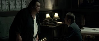 Movie still from “The Outsider” (2018), directed by Martin Zandvliet – Two people in a room with lamps on the wall; Medium shot, Over the shoulder angle