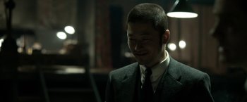 Movie still from “The Outsider” (2018), directed by Martin Zandvliet – A man wearing a suit and tie smiling for the camera; Close Up shot, Over the shoulder angle