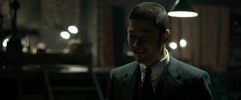 Movie still from “The Outsider” (2018), directed by Martin Zandvliet – A man wearing a suit and tie smiling for the camera; Close Up shot, Over the shoulder angle