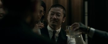 Movie still from “The Outsider” (2018), directed by Martin Zandvliet – A group of people sitting at a table with drinks; Close Up shot, Over the shoulder angle