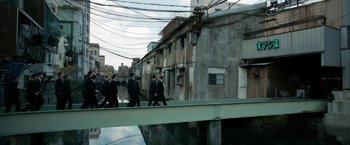 Movie still from “The Outsider” (2018), directed by Martin Zandvliet – A group of men walking across a bridge; Extreme Wide shot, High angle