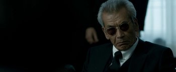 Movie still from “The Outsider” (2018), directed by Martin Zandvliet – An older man wearing a suit and sunglasses; Close Up shot, Low angle