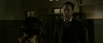 Movie still from “The Outsider” (2018), directed by Martin Zandvliet – A man in a suit and tie standing next to a woman; Medium shot, Over the shoulder angle