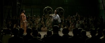 Movie still from “The Outsider” (2018), directed by Martin Zandvliet – A man in a white shirt and a black and white shirt is in front of an audience; Wide shot, Low angle