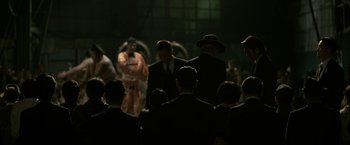 Movie still from “The Outsider” (2018), directed by Martin Zandvliet – A group of men in suits and hats holding umbrellas in a dark room; Wide shot, Over the shoulder angle
