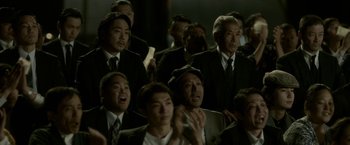 Movie still from “The Outsider” (2018), directed by Martin Zandvliet – A group of men in suits and ties sitting next to each other; Medium shot, Over the shoulder angle