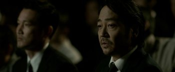 Movie still from “The Outsider” (2018), directed by Martin Zandvliet – A person wearing a suit and tie; Close Up shot, Over the shoulder angle