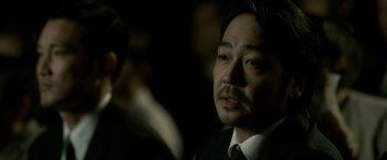 Movie still from “The Outsider” (2018), directed by Martin Zandvliet – A person wearing a suit and tie; Close Up shot, Over the shoulder angle