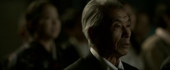 Movie still from “The Outsider” (2018), directed by Martin Zandvliet – An older man in a black suit and white shirt; Close Up shot, Over the shoulder angle