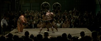 Movie still from “The Outsider” (2018), directed by Martin Zandvliet – Two sumo wrestlers are facing each other in front of an audience; Wide shot, High angle