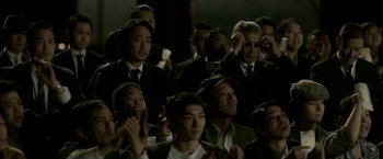 Movie still from “The Outsider” (2018), directed by Martin Zandvliet – A group of men in suits and ties sitting in front of a microphone; Medium shot, Over the shoulder angle