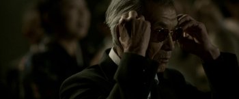 Movie still from “The Outsider” (2018), directed by Martin Zandvliet – An older man wearing a suit and sunglasses; Close Up shot, Over the shoulder angle