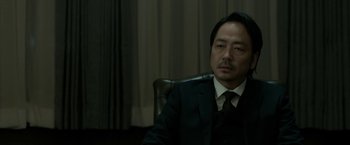 Movie still from “The Outsider” (2018), directed by Martin Zandvliet – A man in a suit and tie sitting in a chair; Close Up shot, Low angle