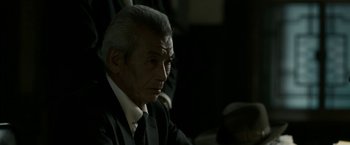Movie still from “The Outsider” (2018), directed by Martin Zandvliet – An older man in a suit and tie looking at the camera; Close Up shot, Over the shoulder angle