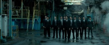Movie still from “The Outsider” (2018), directed by Martin Zandvliet – A group of men in suits standing next to each other in an industrial setting; Wide shot, Low angle