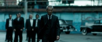 Movie still from “The Outsider” (2018), directed by Martin Zandvliet – A man in a suit and tie walking down a street; Medium shot, Low angle