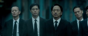 Movie still from “The Outsider” (2018), directed by Martin Zandvliet – Two men in suits and ties standing next to each other; Medium shot, Low angle