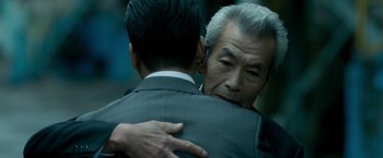 Movie still from “The Outsider” (2018), directed by Martin Zandvliet – A man in a suit hugging another man in a suit; Close Up shot, Over the shoulder angle