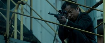 Movie still from “The Outsider” (2018), directed by Martin Zandvliet – A man holding a gun while standing next to a wall; Medium shot, Low angle