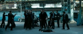 Movie still from “The Outsider” (2018), directed by Martin Zandvliet – A group of men in suits and ties standing around a man laying on the ground; Wide shot, High angle