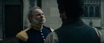Movie still from “The Pale Blue Eye” (2022), directed by Scott Cooper – A man in a military uniform talking to another man in front of a wall; Close Up shot, Over the shoulder angle