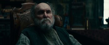 Movie still from “The Pale Blue Eye” (2022), directed by Scott Cooper – An old man with a beard sitting in a chair; Close Up shot, Low angle