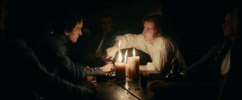 Movie still from “The Pale Blue Eye” (2022), directed by Scott Cooper – A group of people sitting around a table with lit candles; Medium shot, Over the shoulder angle