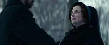 Movie still from “The Pale Blue Eye” (2022), directed by Scott Cooper – An older woman wearing a black hooded jacket; Close Up shot, Over the shoulder angle