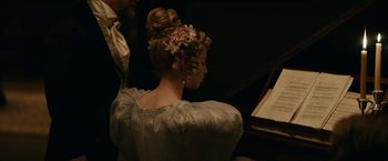 Movie still from “The Pale Blue Eye” (2022), directed by Scott Cooper – A woman in a white dress sitting in front of a piano; Medium shot, Over the shoulder angle