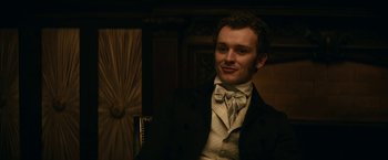 Movie still from “The Pale Blue Eye” (2022), directed by Scott Cooper – A man in a suit and tie standing next to a chair; Close Up shot, Over the shoulder angle