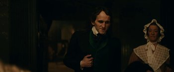 Movie still from “The Pale Blue Eye” (2022), directed by Scott Cooper – A man in a black jacket and green tie; Medium shot, Over the shoulder angle