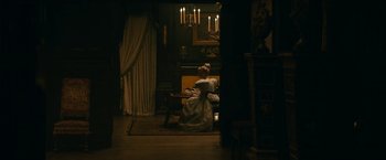 Movie still from “The Pale Blue Eye” (2022), directed by Scott Cooper – A woman sitting on a chair in a living room; Wide shot, High angle