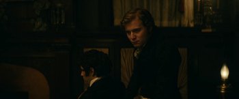 Movie still from “The Pale Blue Eye” (2022), directed by Scott Cooper – A man in a suit and tie next to another man in a suit and tie; Medium shot, Over the shoulder angle