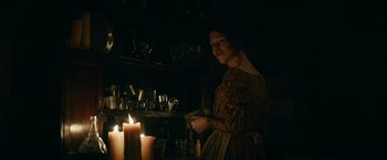 Movie still from “The Pale Blue Eye” (2022), directed by Scott Cooper – A woman standing in front of a lit candle in a dark room; Medium shot, Over the shoulder angle