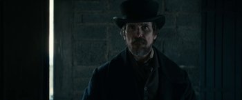 Movie still from “The Pale Blue Eye” (2022), directed by Scott Cooper – A man with a beard wearing a black hat; Medium shot, Over the shoulder angle