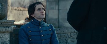 Movie still from “The Pale Blue Eye” (2022), directed by Scott Cooper – A man in a blue jacket is standing next to a stone wall; Close Up shot, Over the shoulder angle