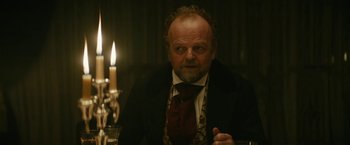 Movie still from “The Pale Blue Eye” (2022), directed by Scott Cooper – An older man in a suit and a tie in front of candles; Close Up shot, Over the shoulder angle