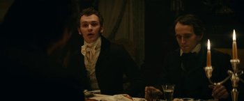 Movie still from “The Pale Blue Eye” (2022), directed by Scott Cooper – A man in a suit sitting at a dinner table; Medium shot, Over the shoulder angle