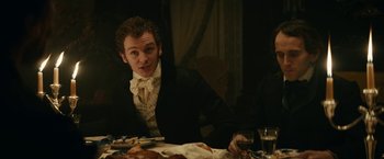 Movie still from “The Pale Blue Eye” (2022), directed by Scott Cooper – A man sitting at a dinner table with food; Medium shot, Over the shoulder angle