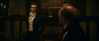 Movie still from “The Pale Blue Eye” (2022), directed by Scott Cooper – A man standing next to another man in front of a fireplace; Medium shot, Over the shoulder angle