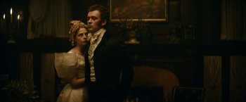 Movie still from “The Pale Blue Eye” (2022), directed by Scott Cooper – A man and a woman standing next to each other in front of a fireplace; Medium shot, Low angle