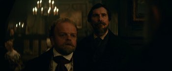 Movie still from “The Pale Blue Eye” (2022), directed by Scott Cooper – Two men standing next to each other in a dark room; Medium shot, Low angle