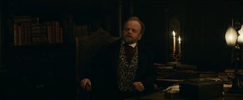 Movie still from “The Pale Blue Eye” (2022), directed by Scott Cooper – A man sitting at a table in a dark room; Medium shot, Low angle