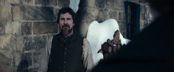 Movie still from “The Pale Blue Eye” (2022), directed by Scott Cooper – A man standing in front of a pile of wood; Medium shot, Over the shoulder angle